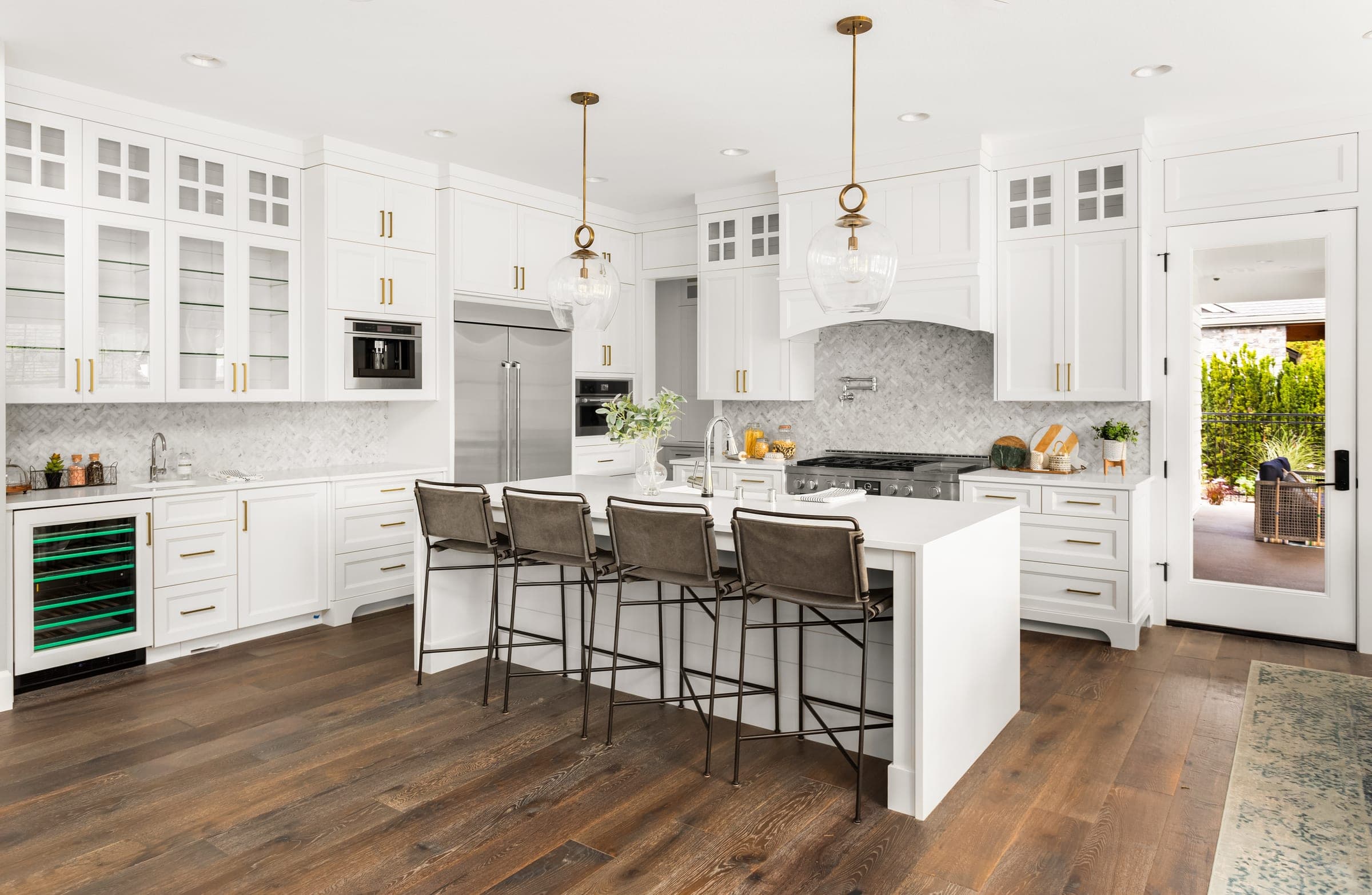 Cali Craft kitchen renovation with white cabinetry, brass pendant lights and a waterfall-edge island over wide-plank flooring