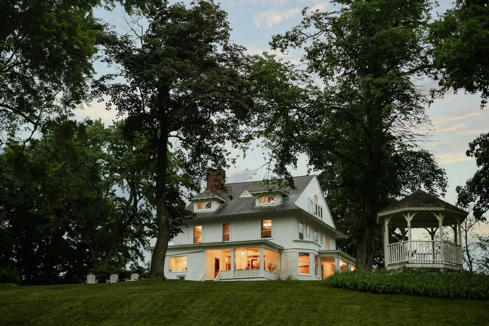 Stock concept image of a white Victorian home with a garden gazebo and lit windows among mature trees — not an actual Cali Craft Renovations project