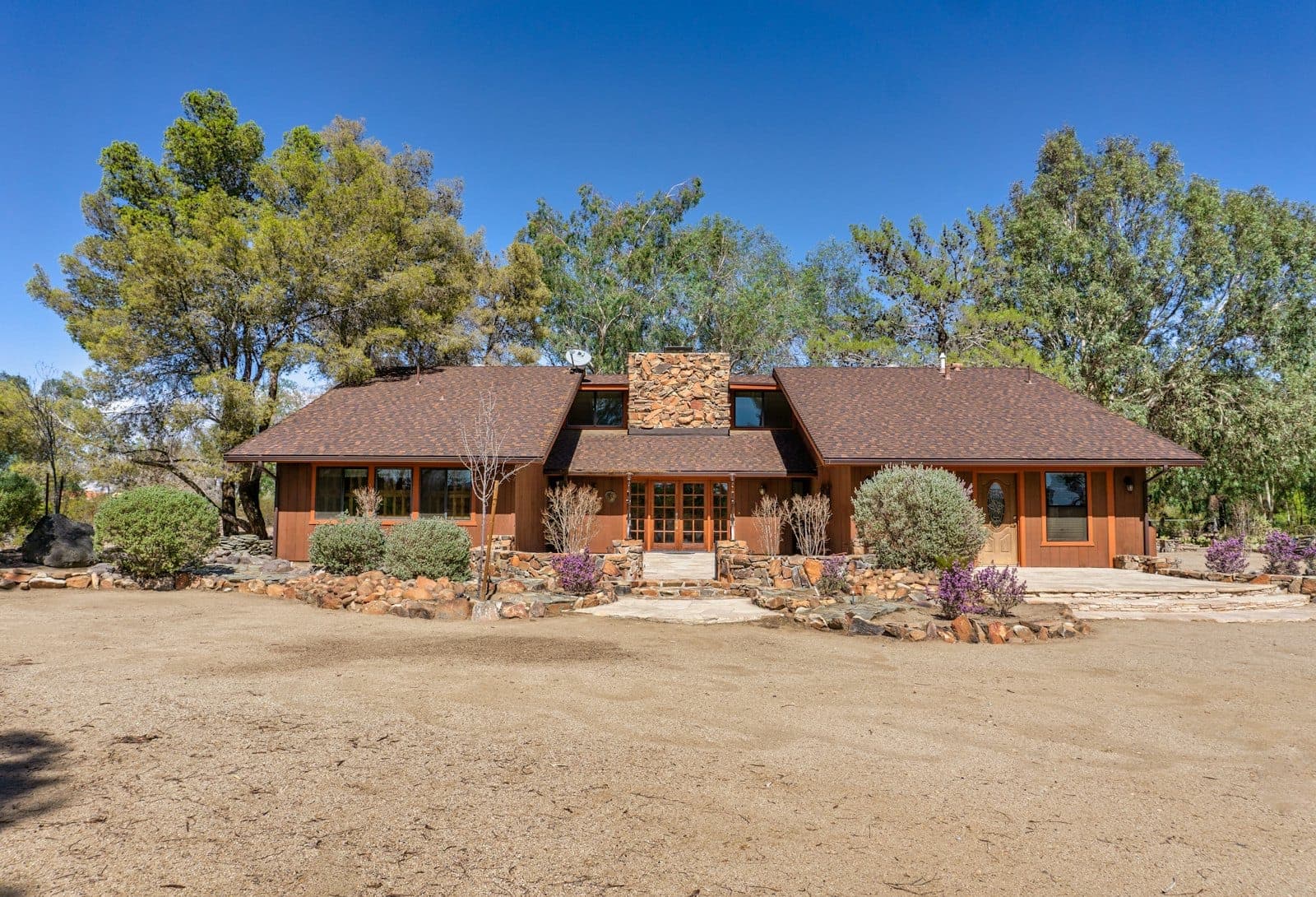 Stock concept image of a low timber ranch home with a stone chimney on a dry, oak-dotted lot — not an actual Cali Craft Renovations project