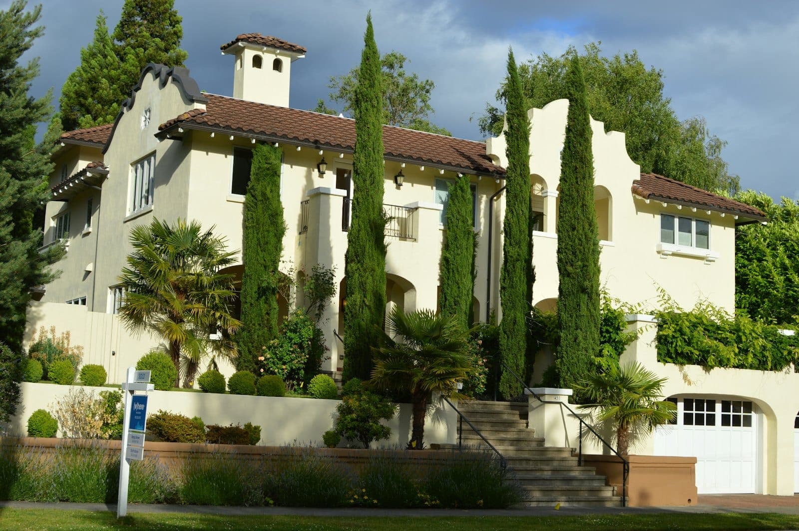 Stock concept image of a Mediterranean-style stucco home with a tile roof and tall cypress trees — not an actual Cali Craft Renovations project