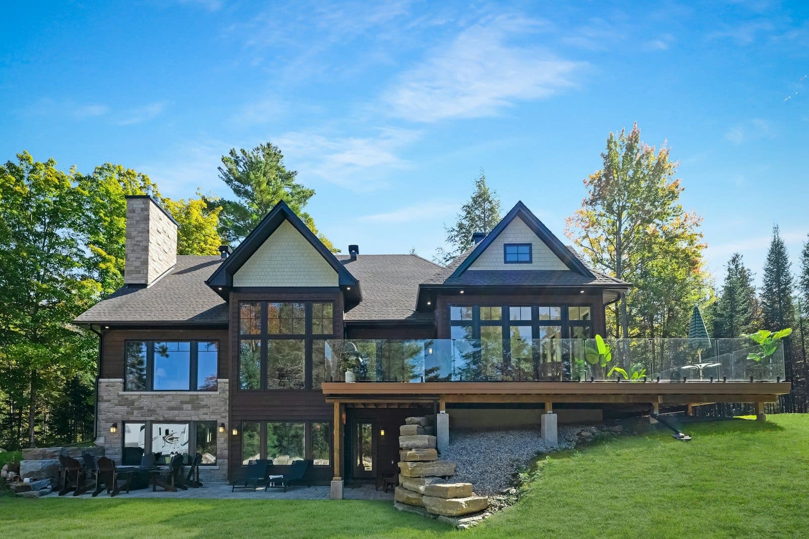 Stock concept image of a custom timber-and-stone home with tall windows on a wooded lot — not an actual Cali Craft Renovations project