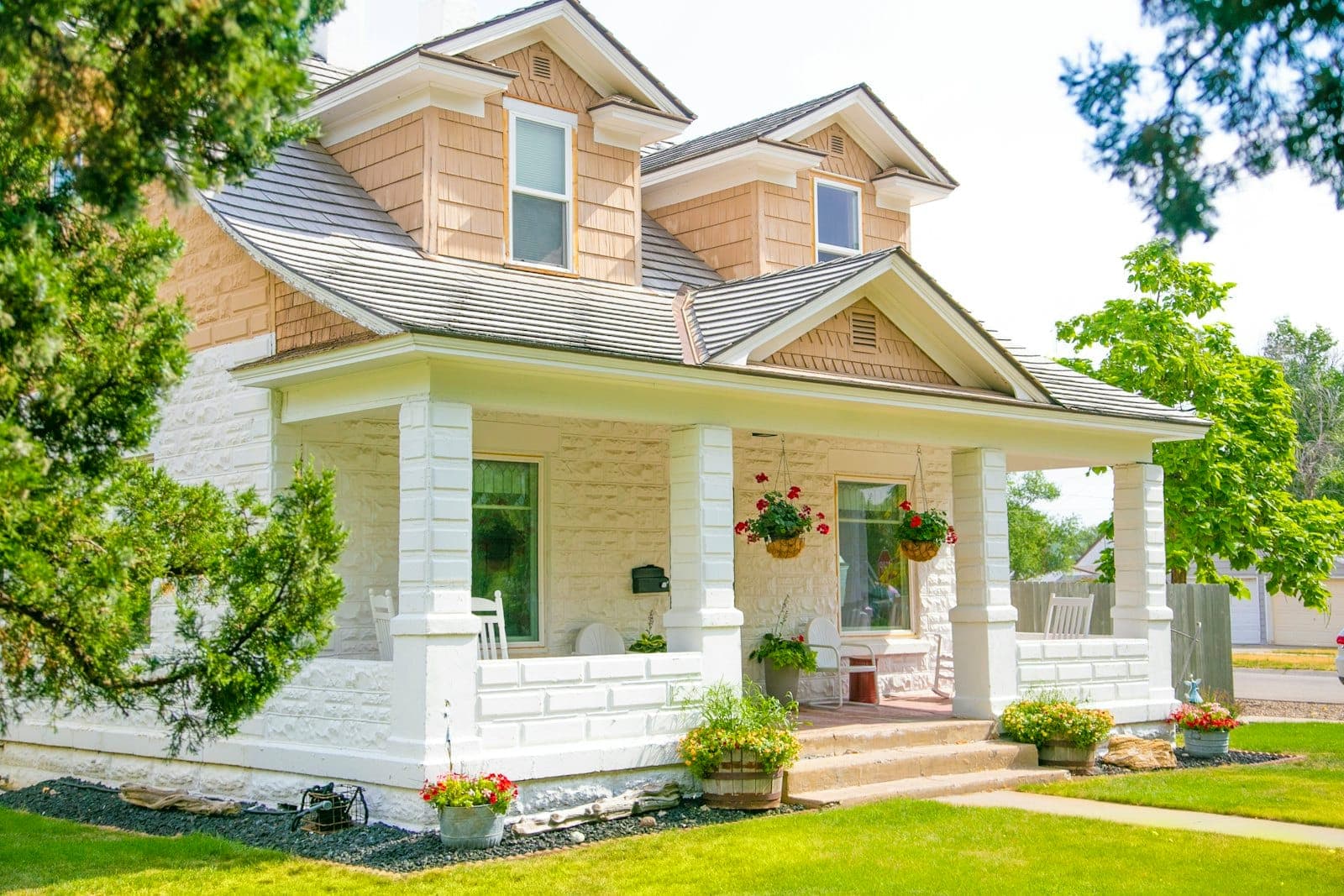 Stock concept image of a Craftsman bungalow with white porch columns and hanging flower baskets — not an actual Cali Craft Renovations project